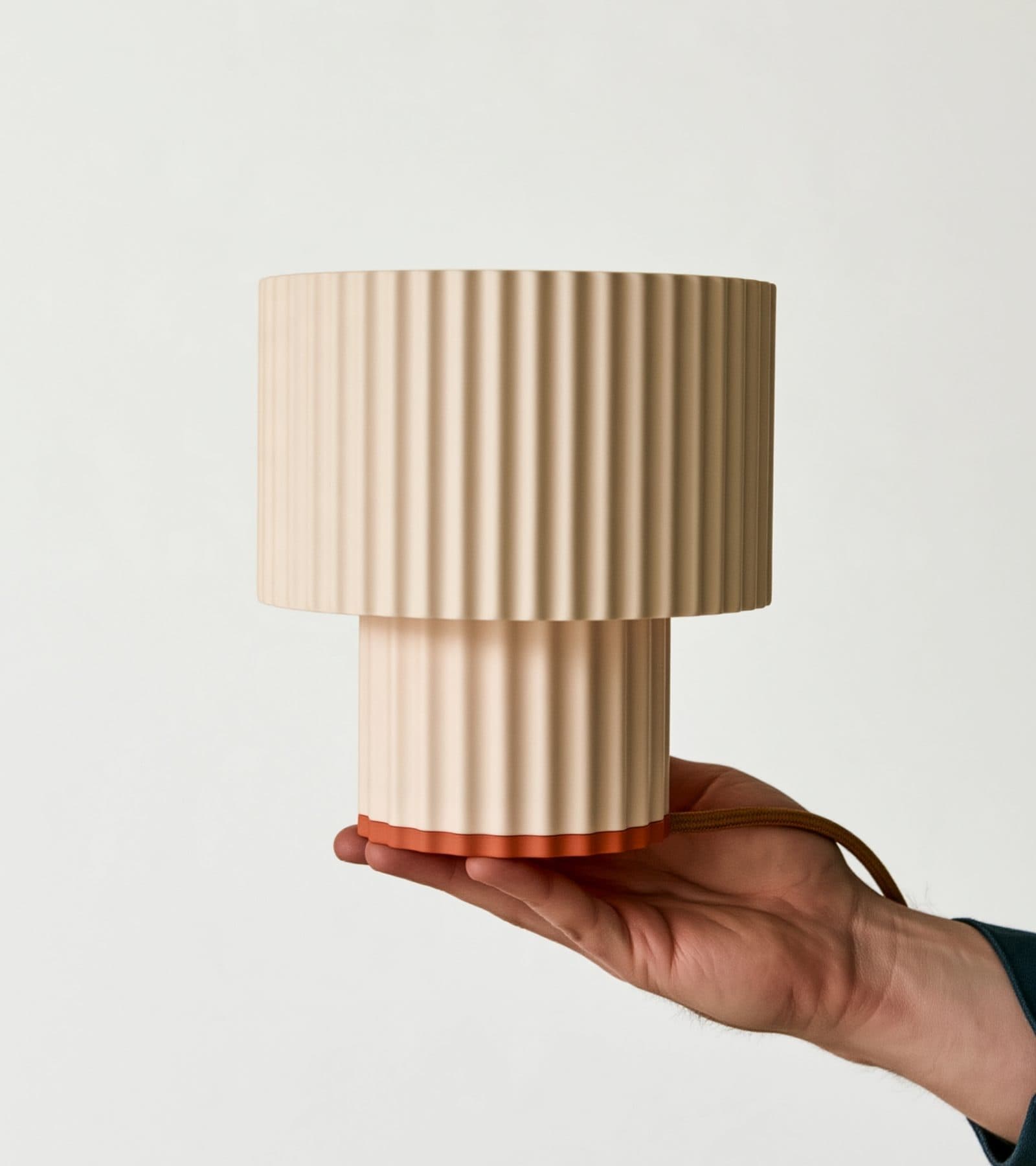 Lámpara Greta crema con base coral, apagada y sostenida en una mano