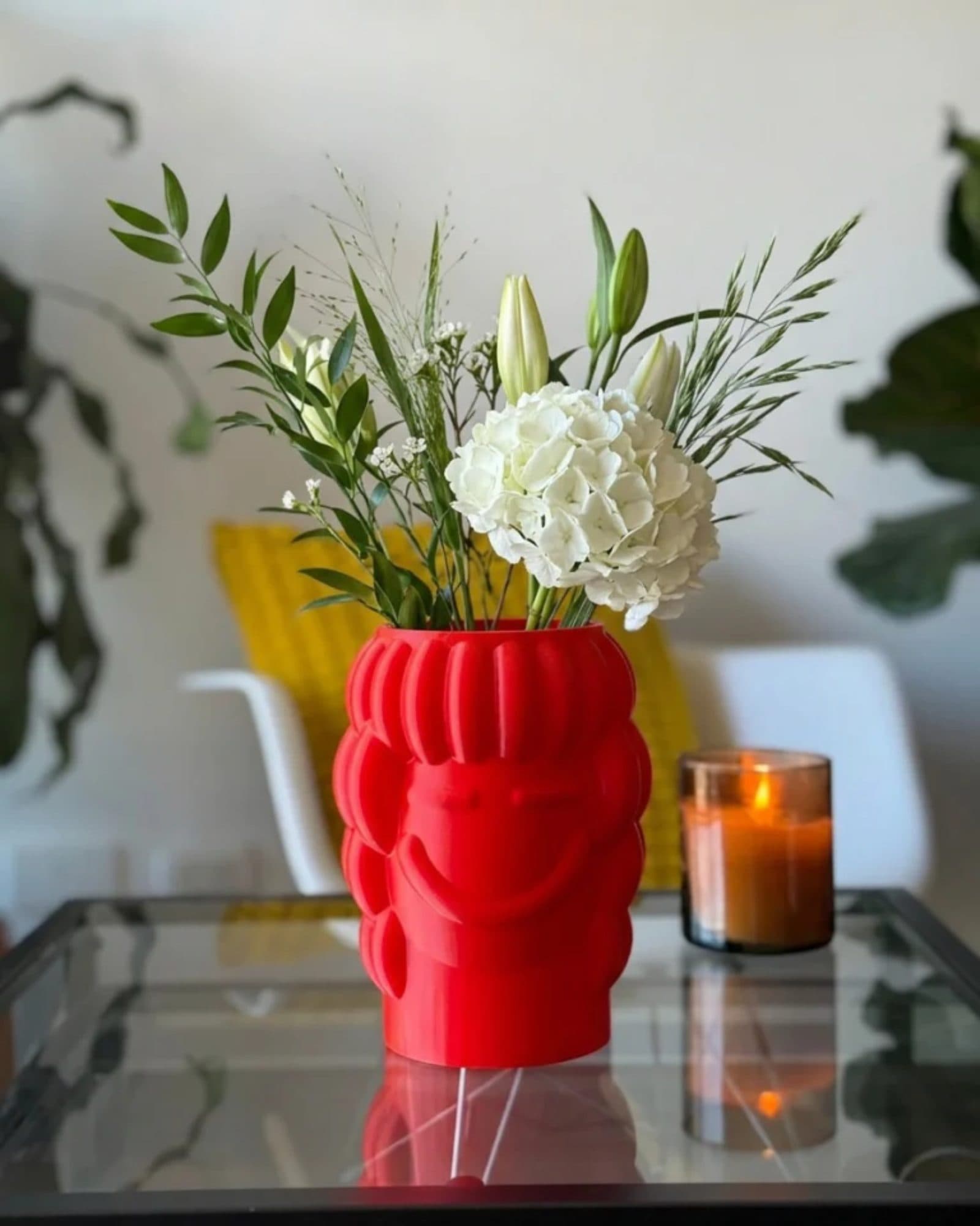 Jarrón Gala rojo con hortensias blancas sobre una mesa de vidrio, junto a una vela